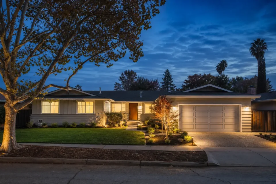 Modern single-story Cambrian ranch home with landscaped front yard, attached garage, and inviting exterior lighting at dusk
